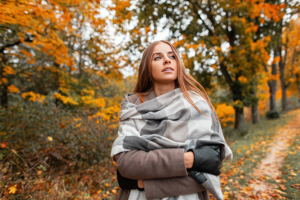 Elegant pretty young woman in fashionable outerwear posing in a forest outside the city. Beautiful girl fashion model resting outdoors in a park. Stylish women's seasonal clothing. Autumn trendy look. - Photo, Image