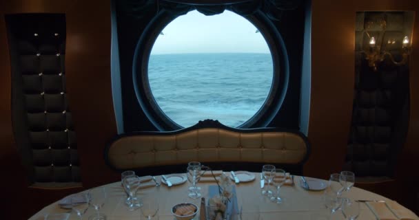 een serveertafel in een restaurant tegen de achtergrond van een enorm rond raam op een cruiseschip. - Video