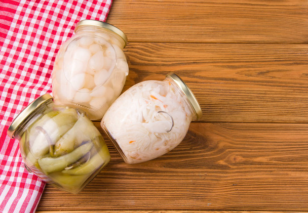 Ζυμωμένα κρεμμύδια, λάχανο και πιπεριές σε ένα βάζο σε ξύλινο τραπέζι. Σπιτικό φαγητό - Φωτογραφία, εικόνα