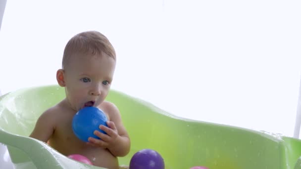 szczęśliwy czysty chłopiec chce wyjść z w kąpieli z kolorowe kulki po kąpieli w jasny pokój - Materiał filmowy, wideo
