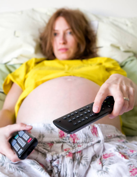 Pregnant woman with remote control - Foto, afbeelding