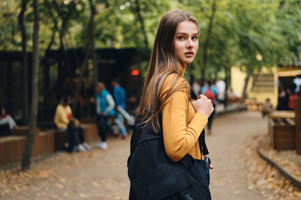 Mooi casual student meisje met rugzak aandachtig op zoek in camera in stadspark - Foto, afbeelding