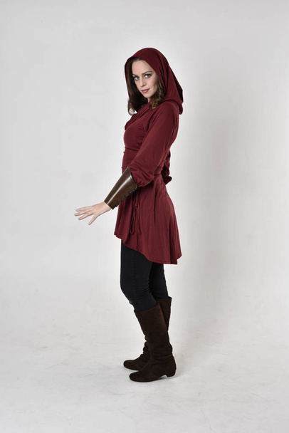 retrato de comprimento total de uma menina morena vestindo uma túnica de fantasia vermelha com capuz. De pé pose em perfil lateral em um fundo de estúdio branco
. - Foto, Imagem