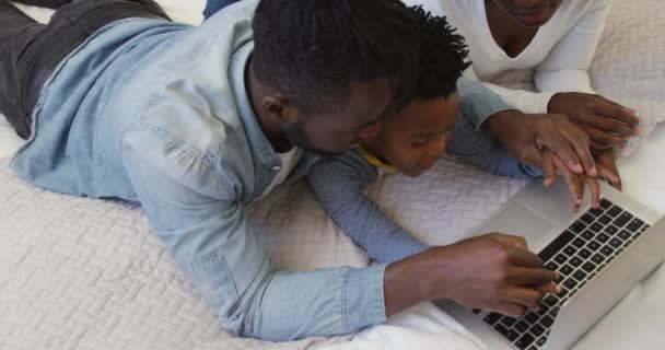 Großaufnahme einer tausendjährigen afrikanisch-amerikanischen Familie und ihres kleinen Sohnes, die zu Hause mit einem Laptop zusammen auf einem Bett liegen, wobei der Vater seinem Sohn beim Tippen auf der Tastatur hilft, Zeitlupe - Filmmaterial, Video