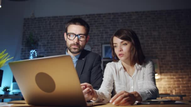Specialists man and woman looking at laptop screen talking in office at night - Footage, Video