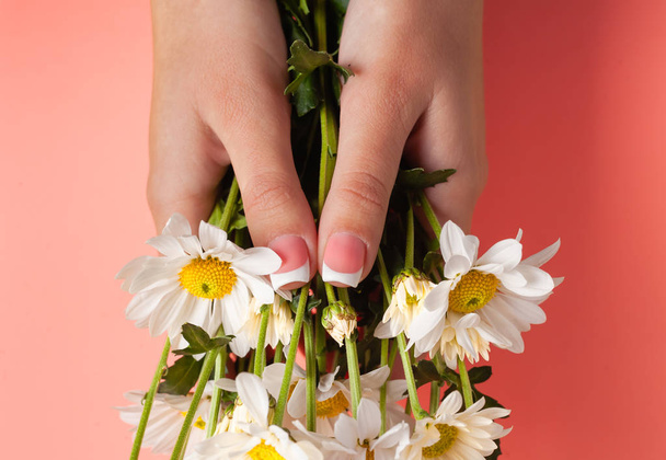 Λεπτά νεαρά χέρια κρατούν λουλούδια, με λεπτό καρπό, καθαρό δέρμα και γαλλικό μανικιούρ. Επίπεδη φωτογραφία lay, με θέση για κείμενο. - Φωτογραφία, εικόνα