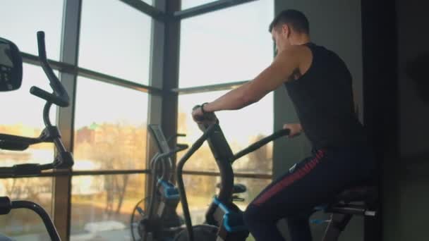 Young active man spinning a air bike in gym with trainers. male training on air bike - Footage, Video