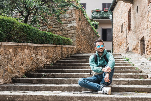 Young traveler sitting on the steps of an old town of San Quirico in Tuscany, Italy - Fotó, kép