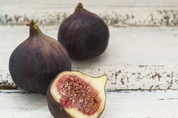Three fresh figs on a wooden white table. One fig is cut in halves and its flesh is visible. Located in a group. - Fotografie, Obrázek
