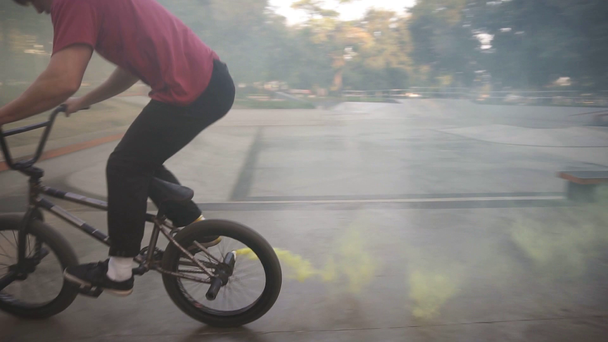 Mladý kavkazský bmx jezdec cvičí v prázdném bruslovém parku, klouže po zábradlí, zatímco žlutá kouřová bomba hoří na zadních kolech. Člověk cvičí triky, jezdí na kole a baví se. Pomalé - Záběry, video