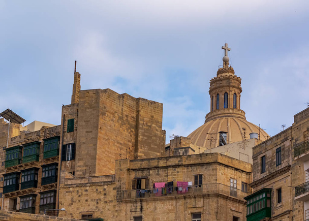 Valletta híres Carmelite templom kupolája mosodai szárítással a lakóház erkélyén az előtérben. Valletta városi élet. - Fotó, kép