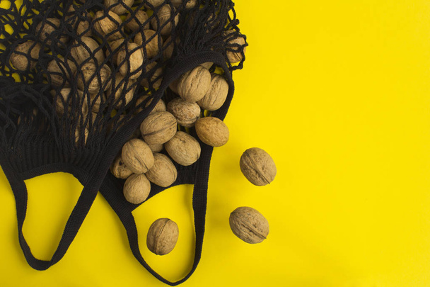 Žádná plastová taška. Mesh nakupování černá taška s vlašskými ořechy na žlutém pozadí. Horní pohled. Kopírovat prostor. - Fotografie, Obrázek