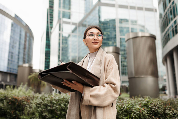 Beautiful businesswoman Asian appearance signs working documents standing right on the street in front of the office - Photo, Image