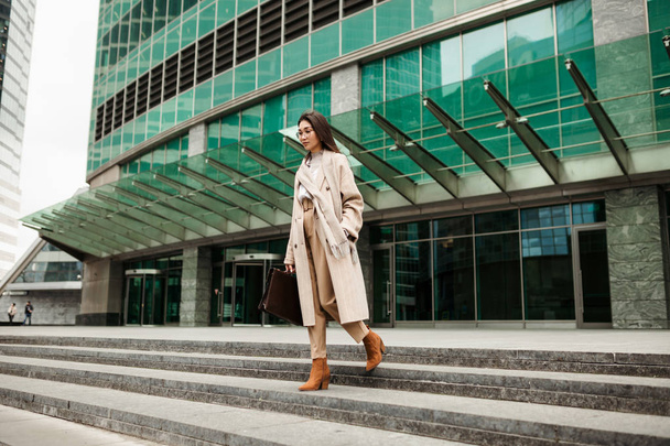 A beautiful Asian lawyer girl with a leather briefcase walks down the steps of the business center - Photo, image