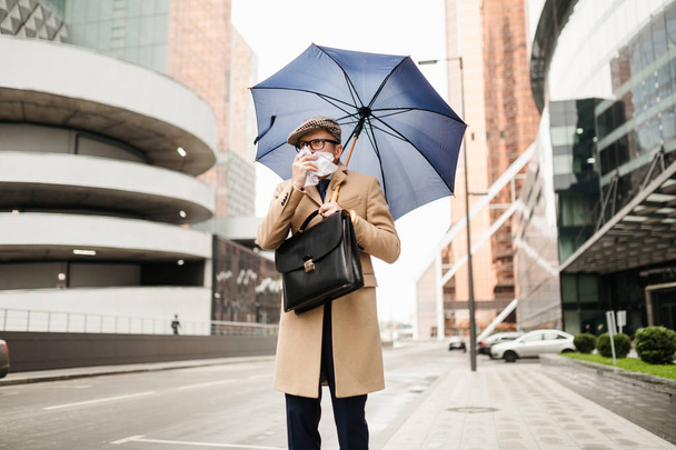 Stylish businessman with an umbrella leaves the office because of a cold - Photo, Image