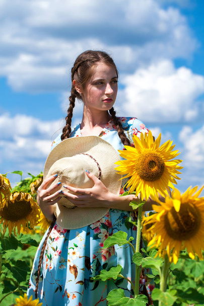 Young beautiful woman in a straw hat in a field of sunflowers - Fotoğraf, Görsel