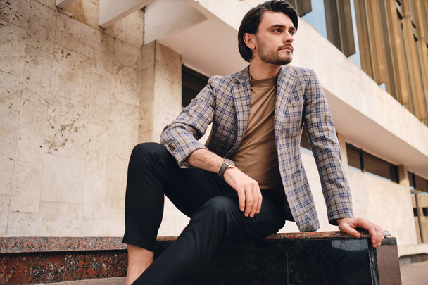Young attractive man in stylish checkered jacket confidently looking away outdoor - Photo, Image