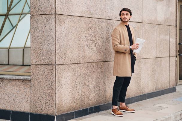 Jeune homme confiant en manteau beige avec lecture de journal regardant vers l'extérieur
 - Photo, image