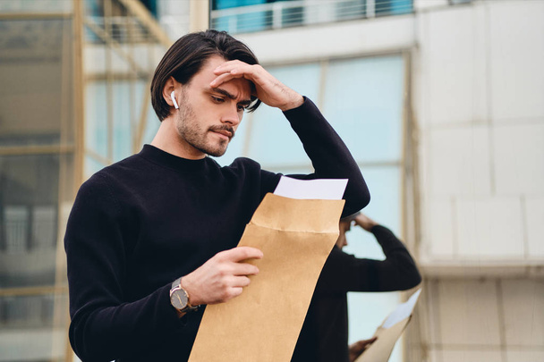 jong triest brunette man bedachtzaam lezen envelop met reactie outdoor - Foto, afbeelding