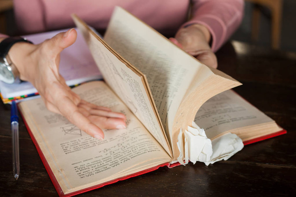 Vrouwelijke handen met nette manicure en een groot klokkenblad door een dik boek met veel bladwijzers op tafel. - Foto, afbeelding