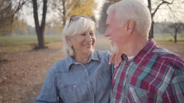 Happy Caucasian mature family looking at each other and smiling. Senior European couple standing in sunlight in autumn park. Husband and wife spending evening outdoors. Aging together, eternal love. - Video