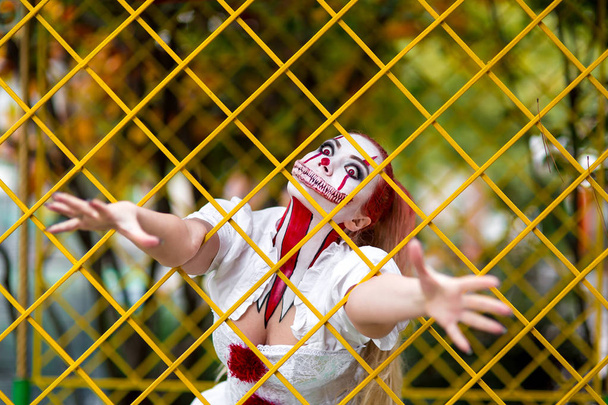 девушка в образе ужаса для празднования Хэллоуина с макияжем клоуна пенис и мрачные зубы яда, портрет сумасшедшей женщины в белом платье с оранжевыми волосами
. - Фото, изображение