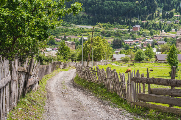 Camino de tierra por la ladera a lo largo de las vallas de madera, en la parte superior de Mestia. Región de Svaneti, Georgia
. - Foto, imagen