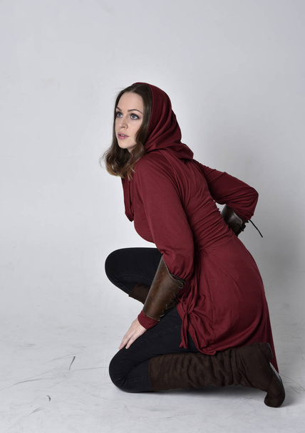 retrato de comprimento total de uma menina morena vestindo uma túnica de fantasia vermelha com capuz. Sentado posar em um fundo de estúdio branco
. - Foto, Imagem