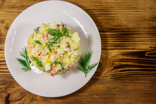 Salade avec bâtonnets de crabe, maïs sucré, concombre, œufs et mayonnaise sur table en bois. Vue du dessus - Photo, image