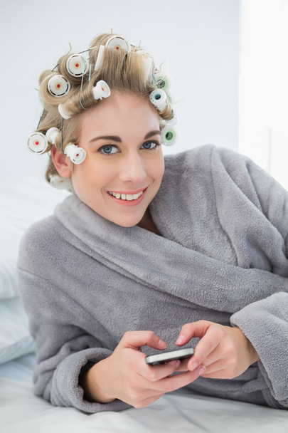 Joyful relaxed blonde woman in hair curlers using her mobile phone - Foto, Imagem