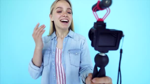 Piękna dziewczyna blogger odciąża się na kamerze odizolowane niebieskie tło - Materiał filmowy, wideo