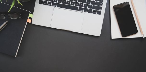 Draufsicht auf dunklen modernen Arbeitsplatz mit Laptop und Bürobedarf auf schwarzem Tischhintergrund  - Foto, Bild