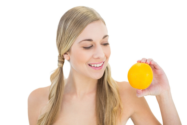 Pleased young blonde woman looking at an orange - Foto, Imagem