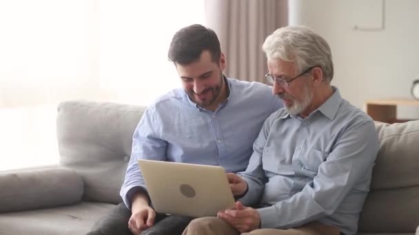 Elderly father and son sitting on couch laughing watching video - Séquence, vidéo