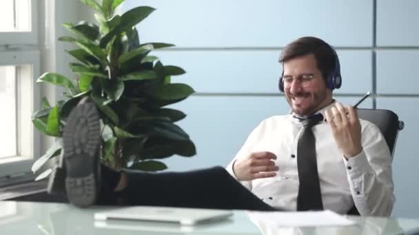 Businessman wearing headphones imitating playing guitar enjoy music during break - Materiał filmowy, wideo