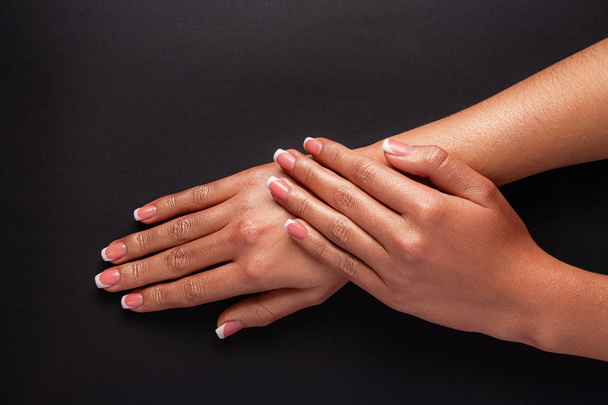 The hands of a young girl are covered with a highlight top. French manicure. Hands on a black background. - Foto, Bild