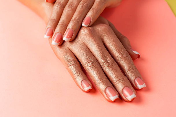 Stylish trendy french manicure. Hands of a beautiful young woman are covered by highlight on a pink background. - Photo, Image