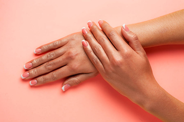 Stijlvolle trendy Franse manicure. Handen van een mooie jonge vrouw zijn bedekt door hoogtepunt op een roze achtergrond. - Foto, afbeelding