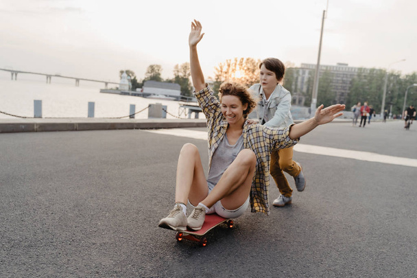 Alegre filho montando sua mãe em um skate e rindo
. - Foto, Imagem