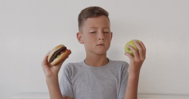 Boy choosing healthy or unhealthy food. Boy making a choice between apple and burger, healthy or fast, junk food, chose apple. Useful or harmful lifestyle. - Video, Çekim