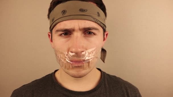 homem refém com uma boca gravada em um fundo bege
 - Filmagem, Vídeo