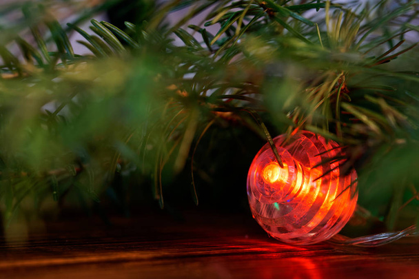 Hämmästyttävä punainen valoisa pallo sijaitsee joulukuusen oksan alla
  - Valokuva, kuva