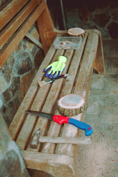 um velho martelo, uma serra de mão, luvas protetoras e um feixe de pinheiro redondo com serragem em um banco. Suporte de madeira para comida para a master class. Conceito DIY
. - Foto, Imagem