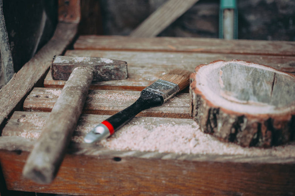 an old rusty hammer, a paint brush and a round pine beam with sawdust on a bench. Wooden stand for food for the master class. DIY concept. - Fotó, kép