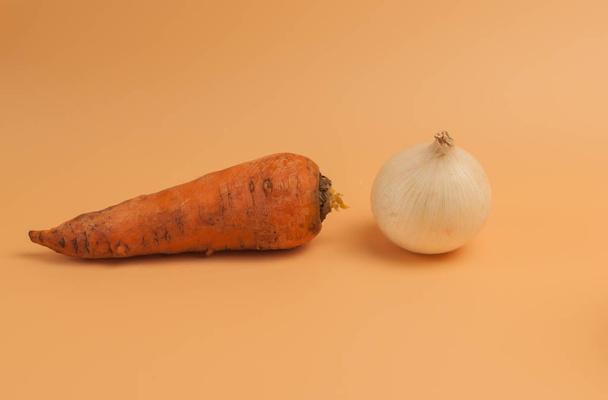 organic carrots and onions on a beige background, unpeeled sweet carrots and onions on the surface, vegetables from the garden in a minimalist style, vitamins, vegetarian food,healthy eating concept. - Foto, imagen