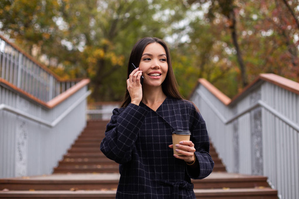 若いですかなりカジュアルな女性でコーヒーと一緒に携帯電話で楽しく公園を歩く話を行く - 写真・画像
