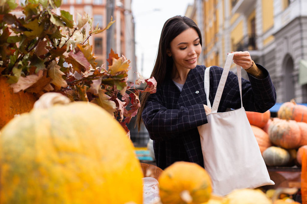 Young attractive casual woman happily buying pumpkin at autumn farm shop outdoor - Photo, Image