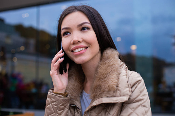 Retrato de una joven hermosa mujer con chaqueta abajo felizmente hablando por teléfono celular en la calle de la ciudad
 - Foto, imagen
