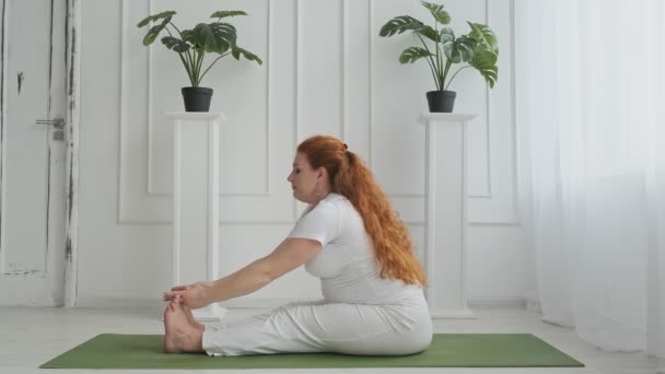 Beautiful mother practicing yoga in white apartment sitting on green mat in UHD - Imágenes, Vídeo