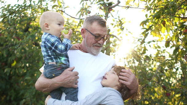 Szakállas, érett férfi egy kisgyerekkel a karjában és egy tinédzser fiú ölelésével és csókjával, boldog család. Nagyapa és két unoka. - Felvétel, videó